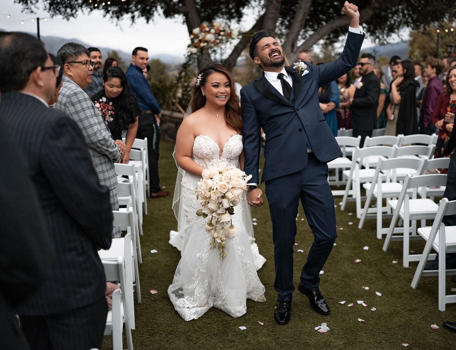 Wedding ceremony recessional with white chairs and confetti toss in outdoor garden setting.