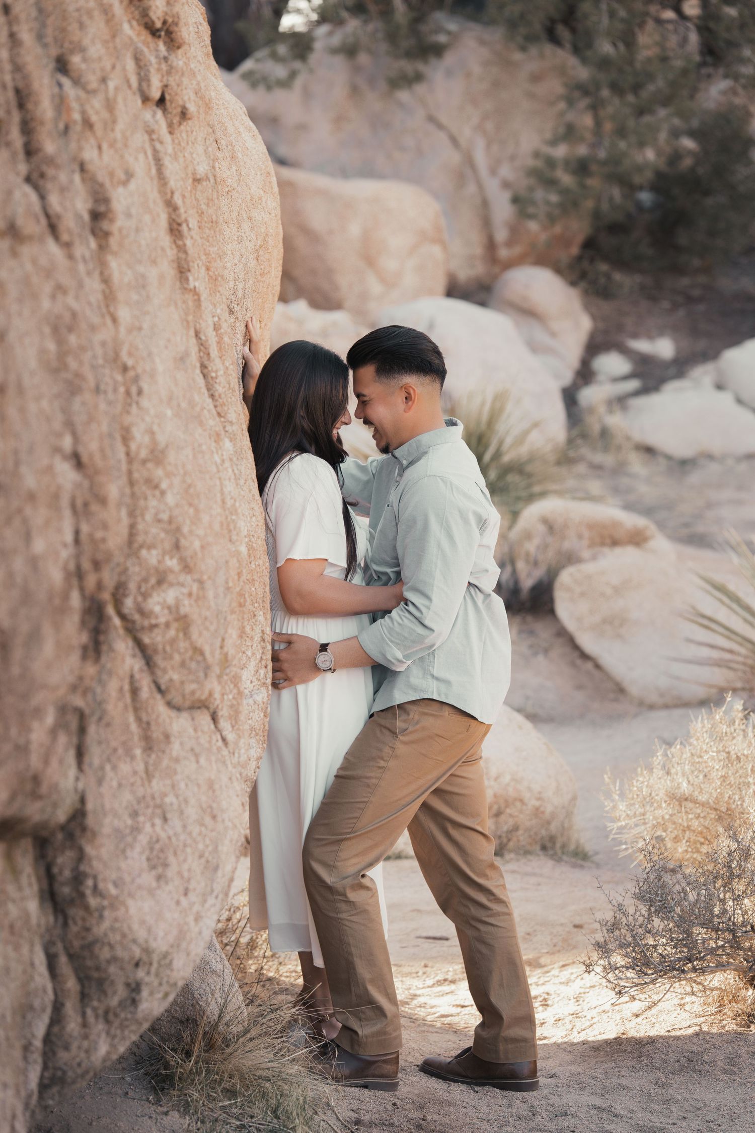 A couple shares a tender moment against a rocky desert wall in casual attire.