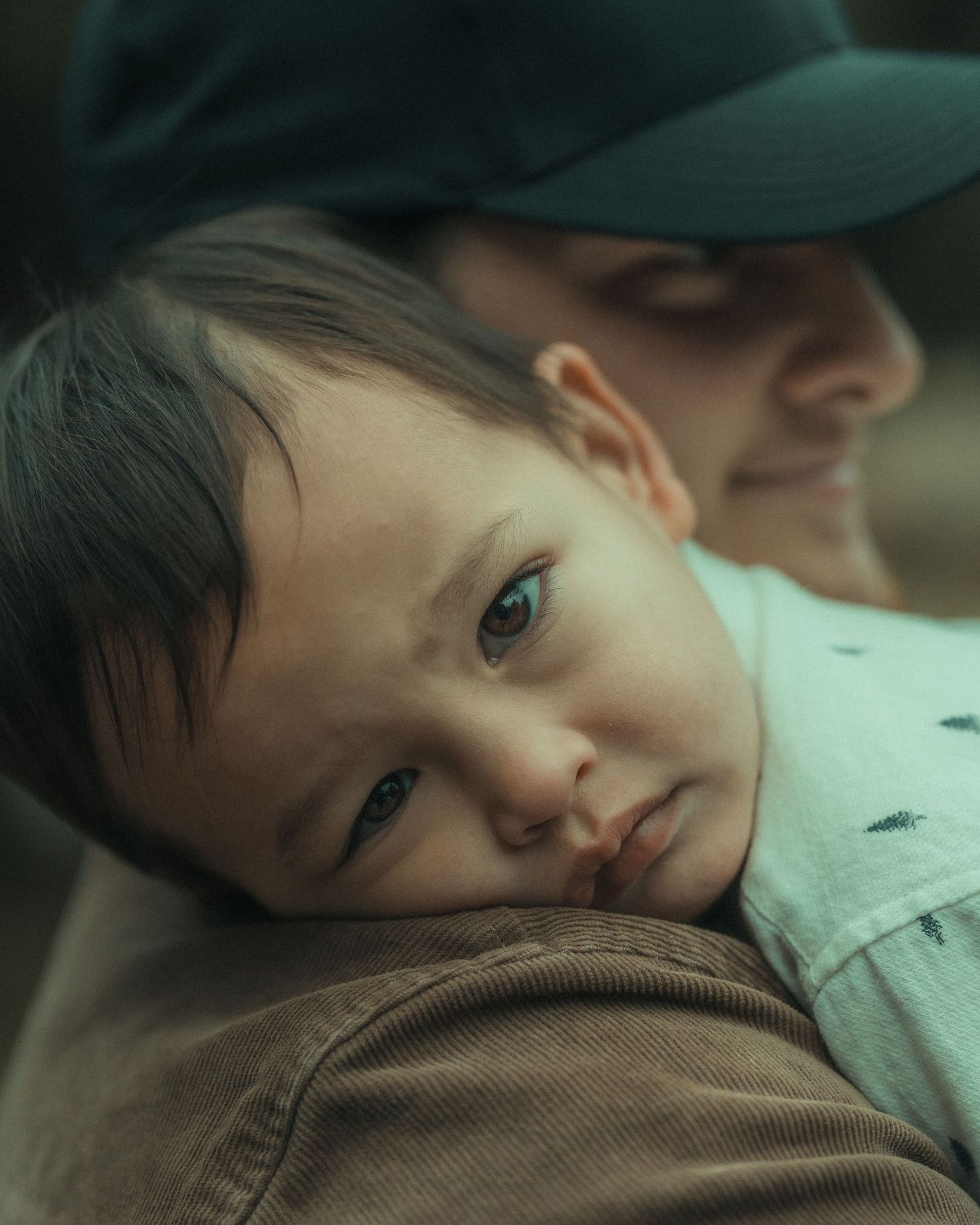 Child resting peacefully against someone wearing a brown jacket.