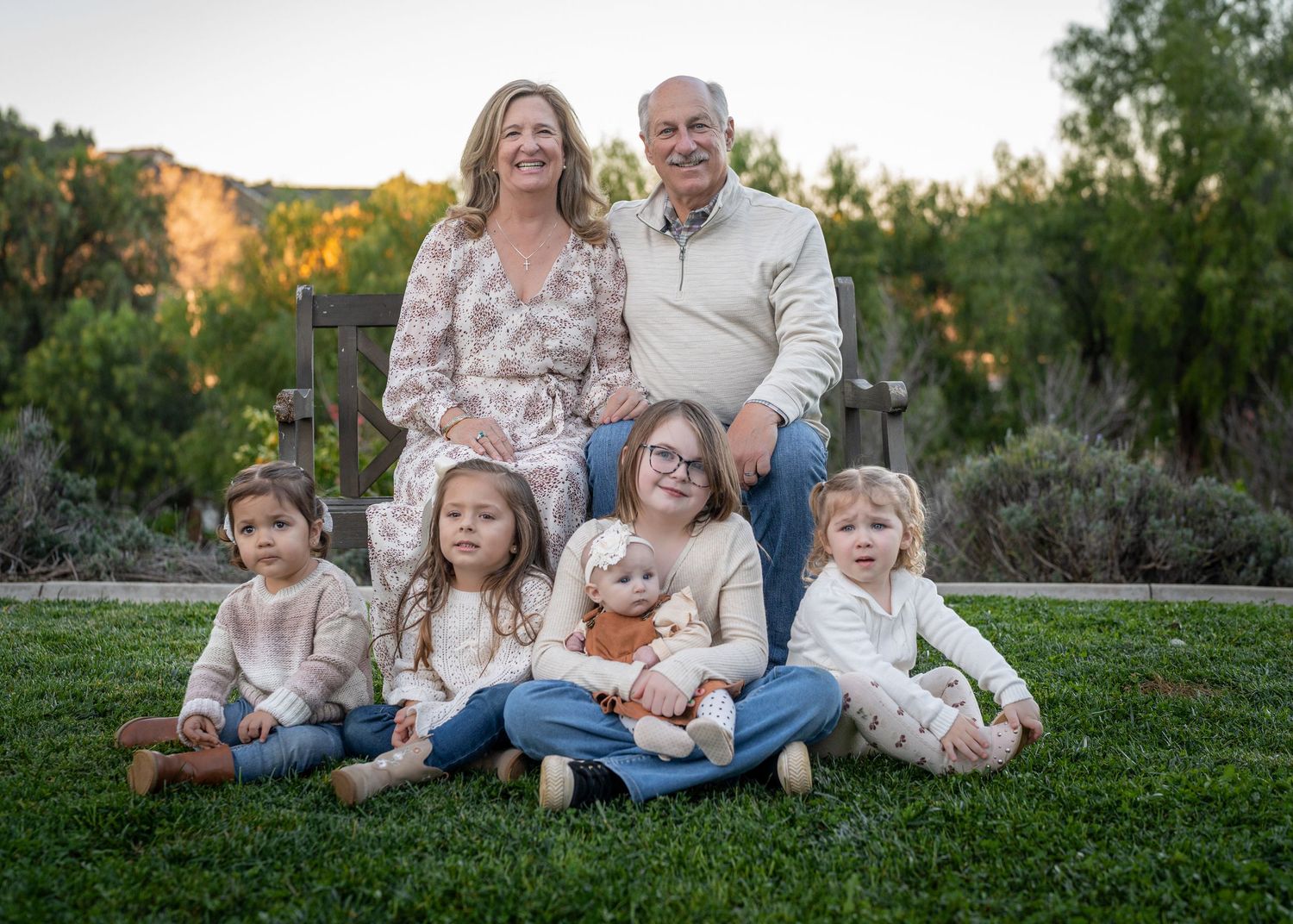 Family group portrait on grass with natural landscape and trees in the background during golden hour.