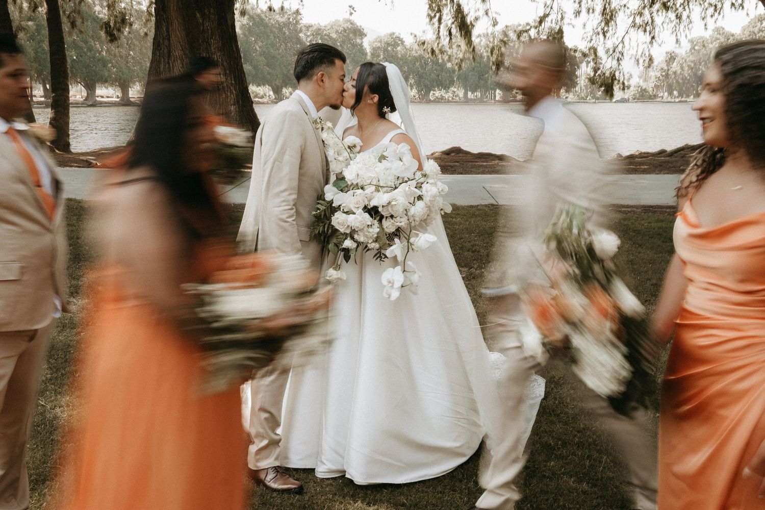 Romantic outdoor wedding ceremony with bridesmaids in peach dresses and white floral arrangements under oak trees.