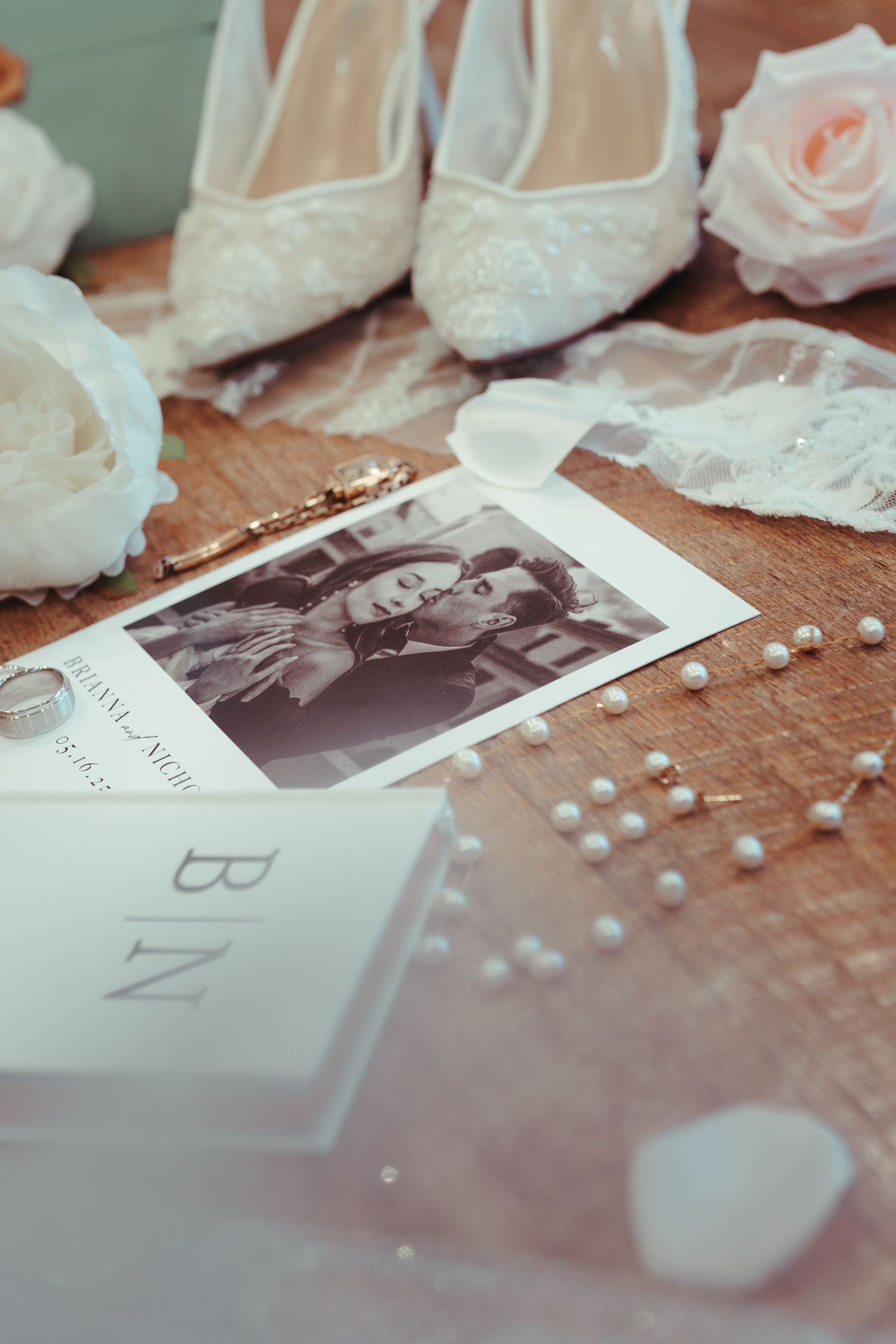 Wedding details including lace accessories and vintage photographs arranged on wooden surface.