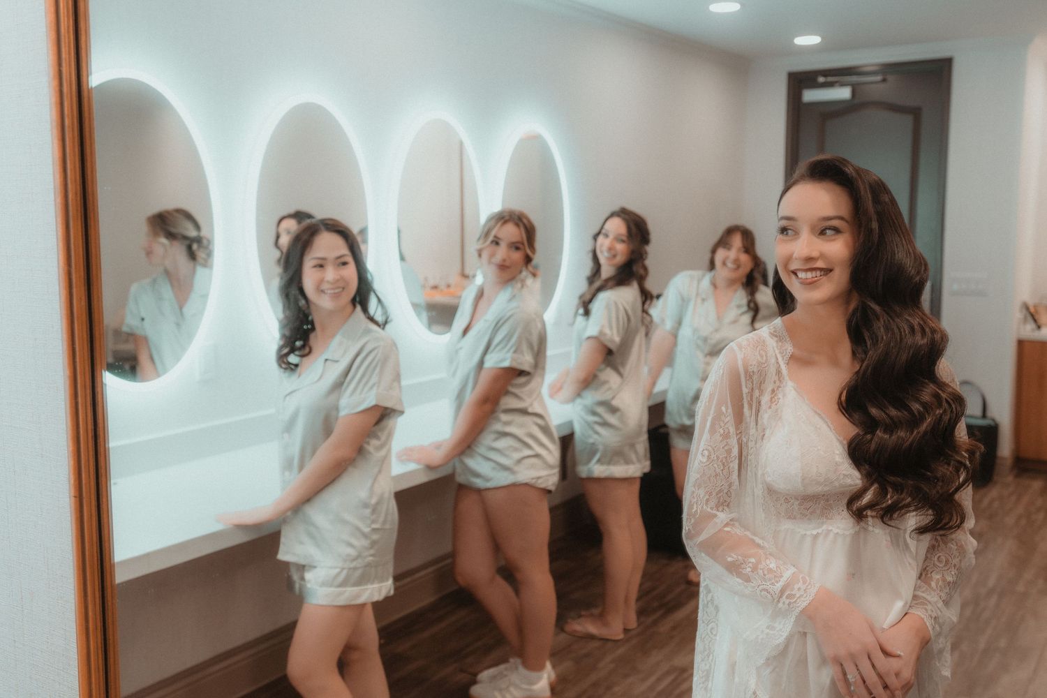 Bridal party in white robes celebrating in bright indoor setting.
