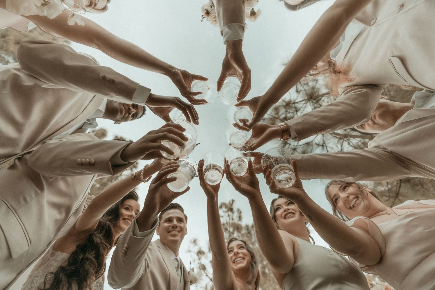 Wedding party forms a joyful circle with a toast during outdoor celebration.