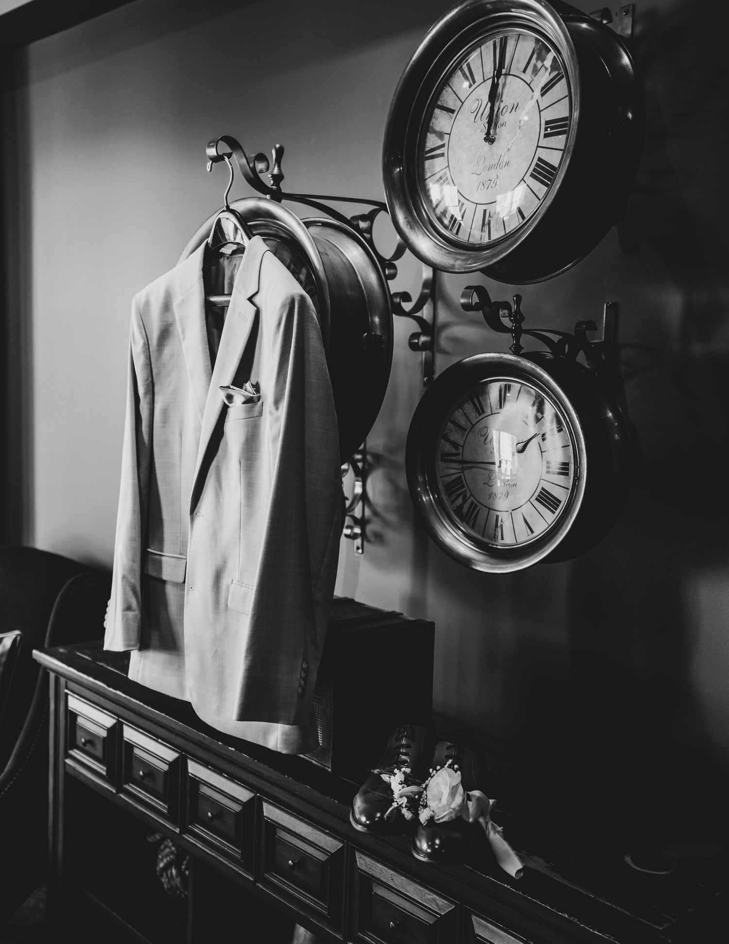 Vintage clocks and white clothing displayed against a dark wall in moody black and white.