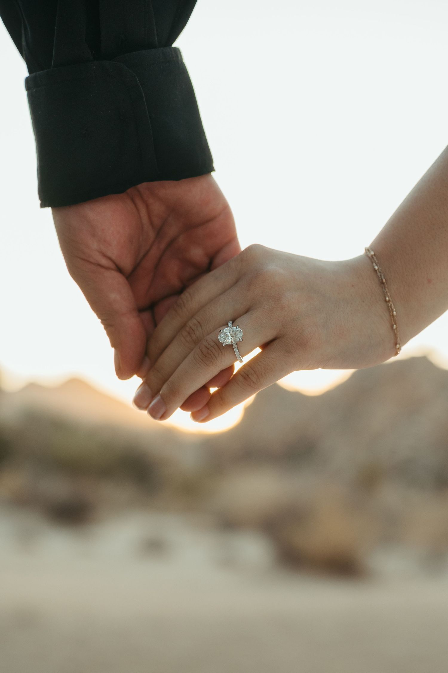 Close-up of engaged couple holding hands with engagement ring in golden sunlight.