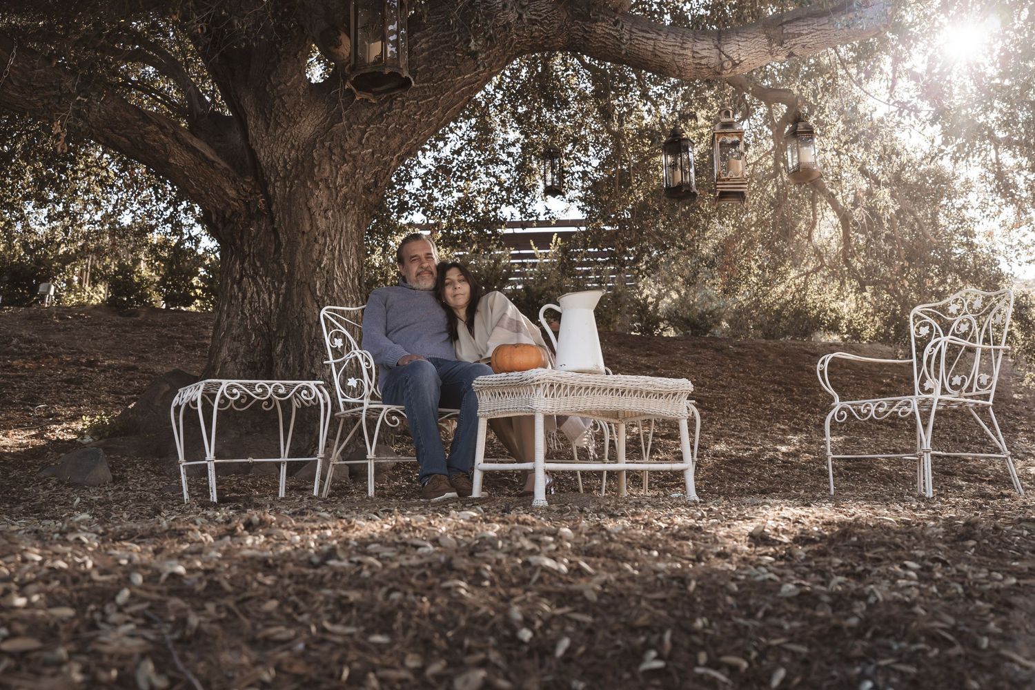 Romantic outdoor photoshoot on rustic white bench with sunlight filtering through trees.