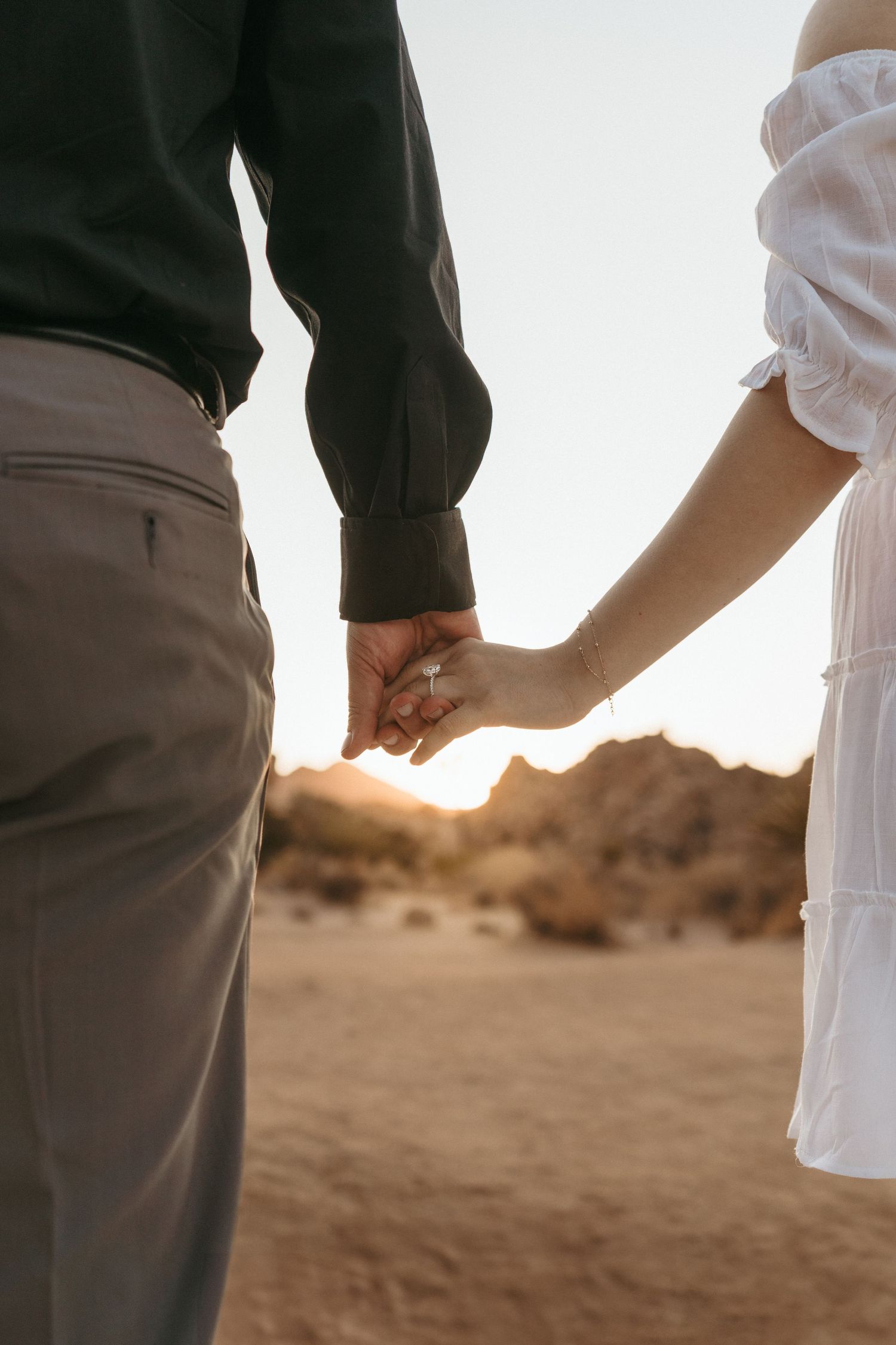 Close-up of couple's hands touching during sunset in a desert setting.