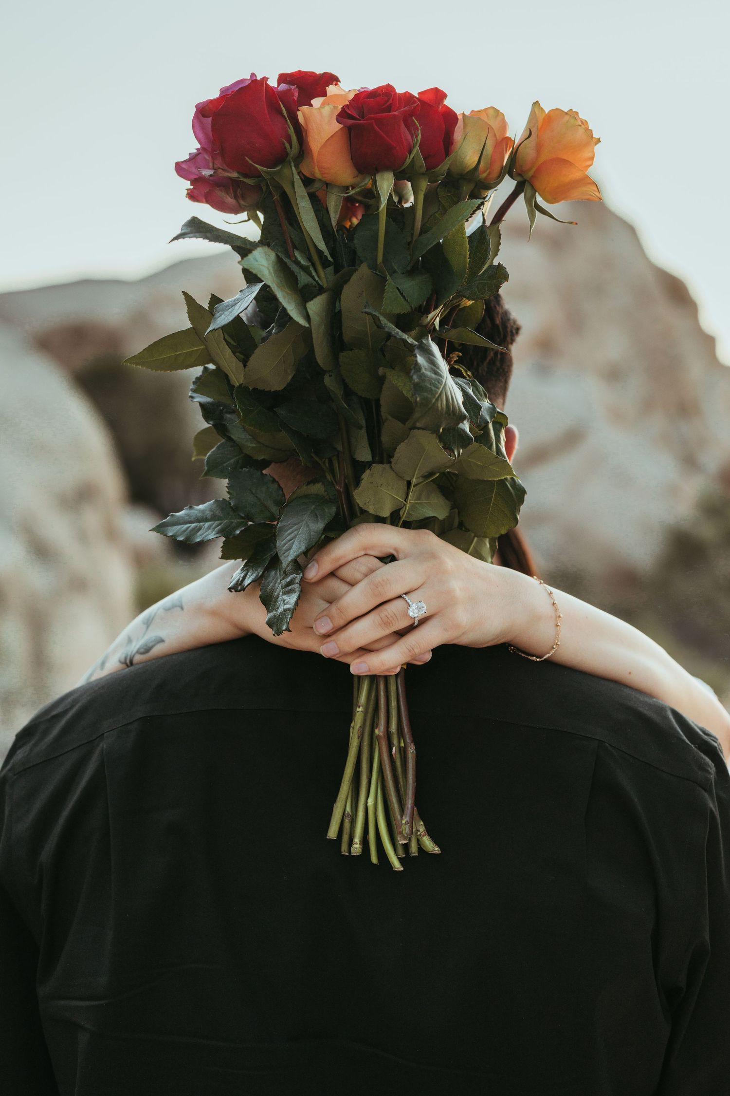 A bouquet of red and orange roses held against a black shirt in natural lighting.