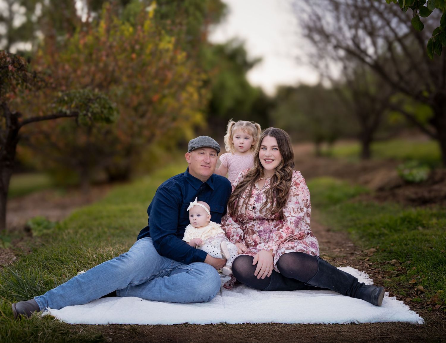 Family lounging on white blanket during outdoor photo session.
