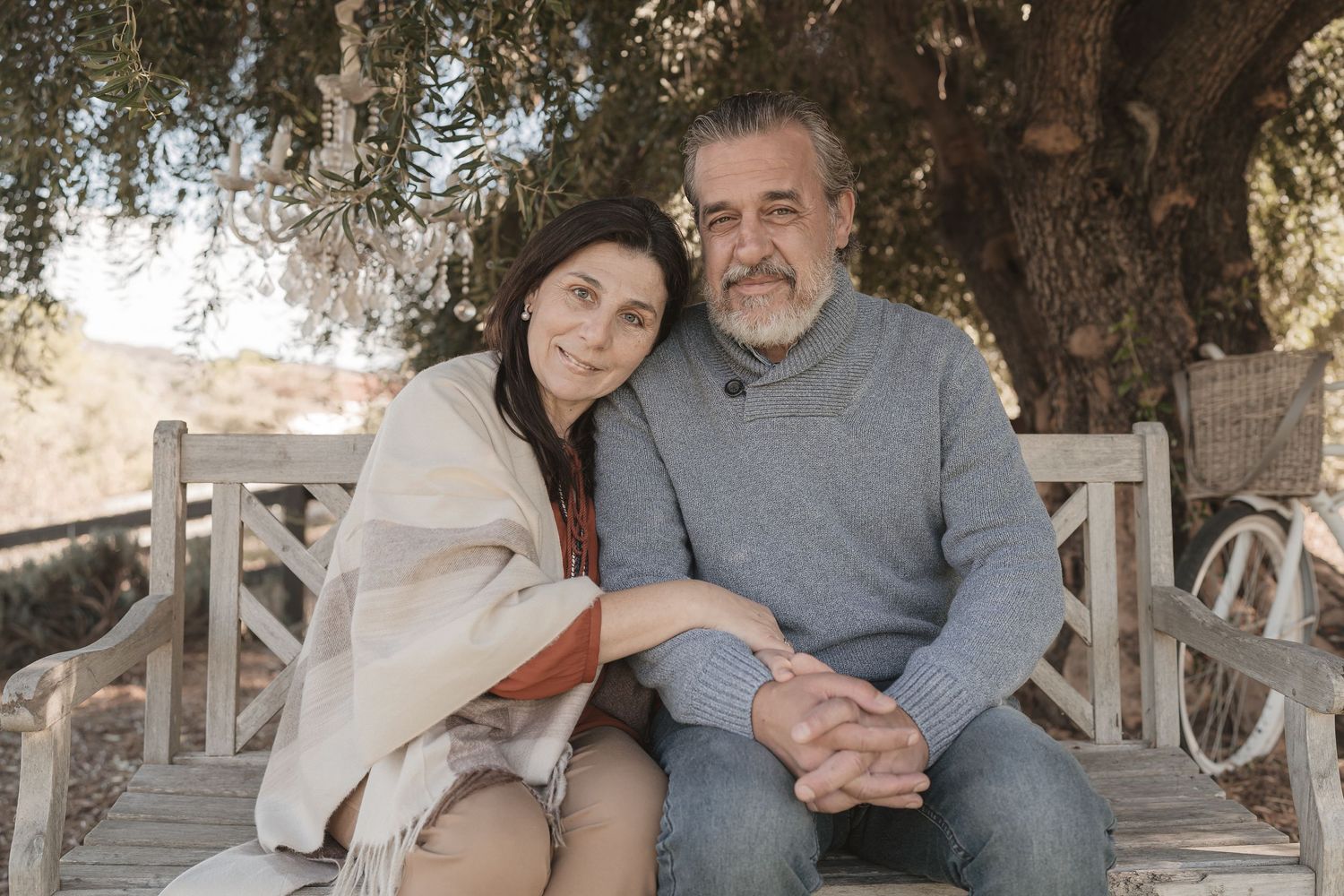 Couple sitting together on a white bench under a tree in natural outdoor setting.