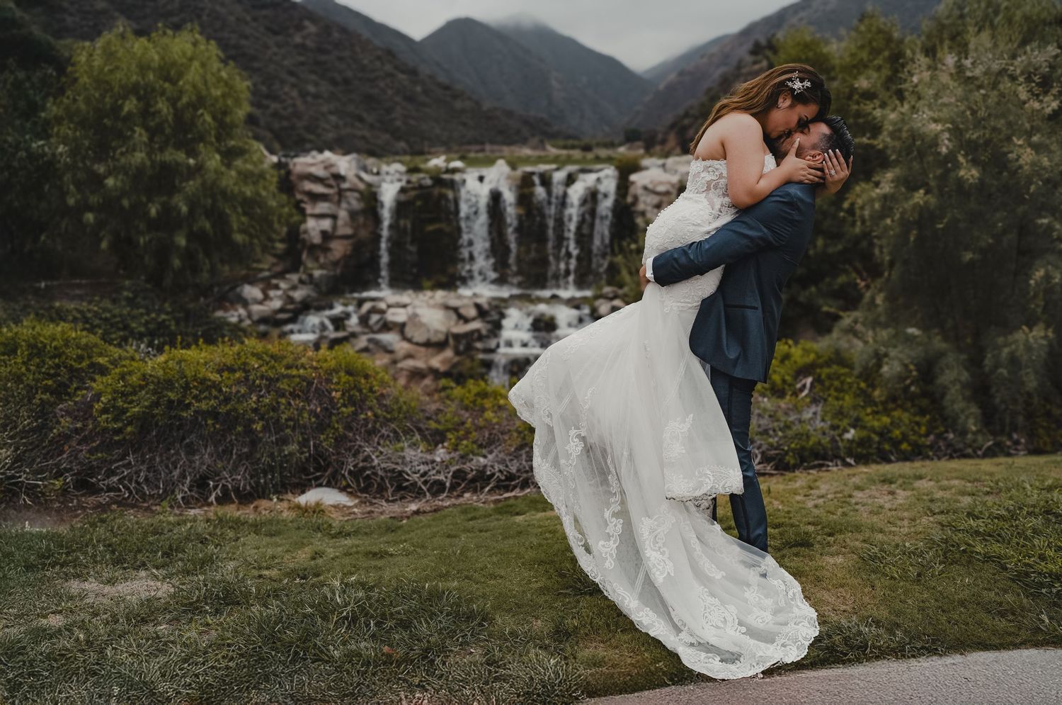 Scenic mountain landscape serves as backdrop for wedding photos with waterfall in distance.