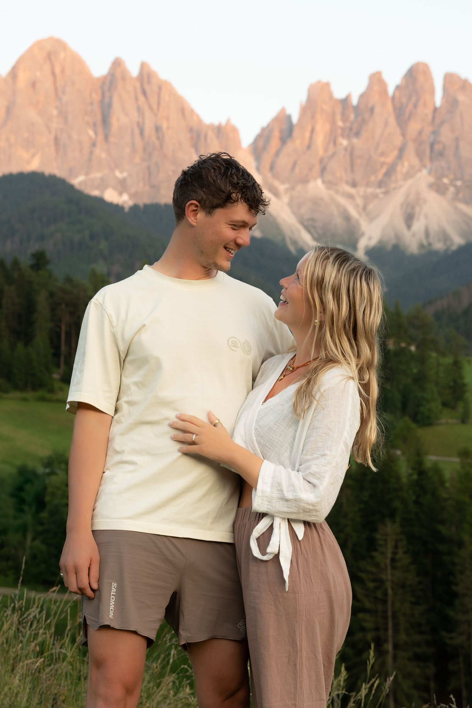Couple in casual attire embracing in a meadow with dramatic Dolomite mountains in background.