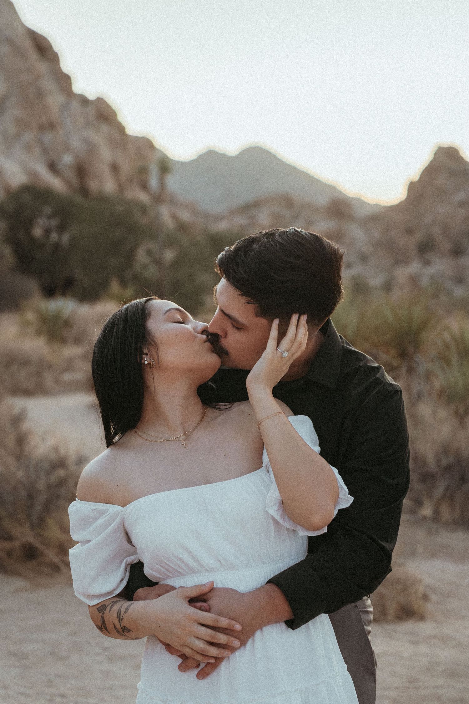 Romantic desert engagement session with couple embracing at sunset among rocky terrain.