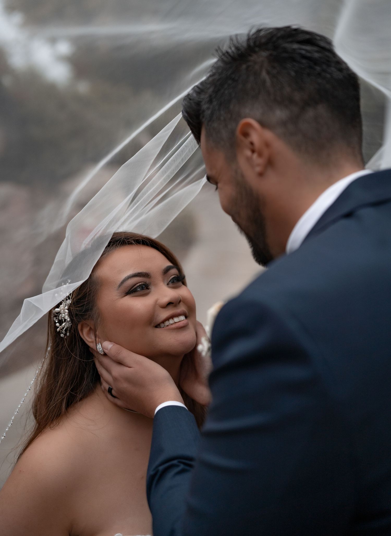 Close-up of tender wedding moment with bride's veil flowing in natural light.