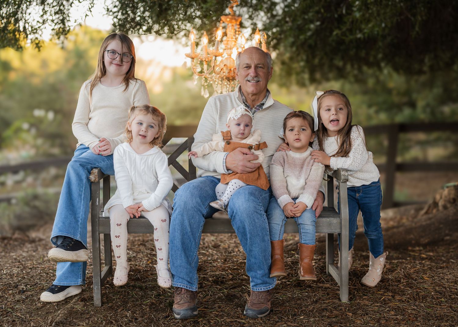 Family members sitting casually on a wooden bench surrounded by fallen leaves in an outdoor setting.