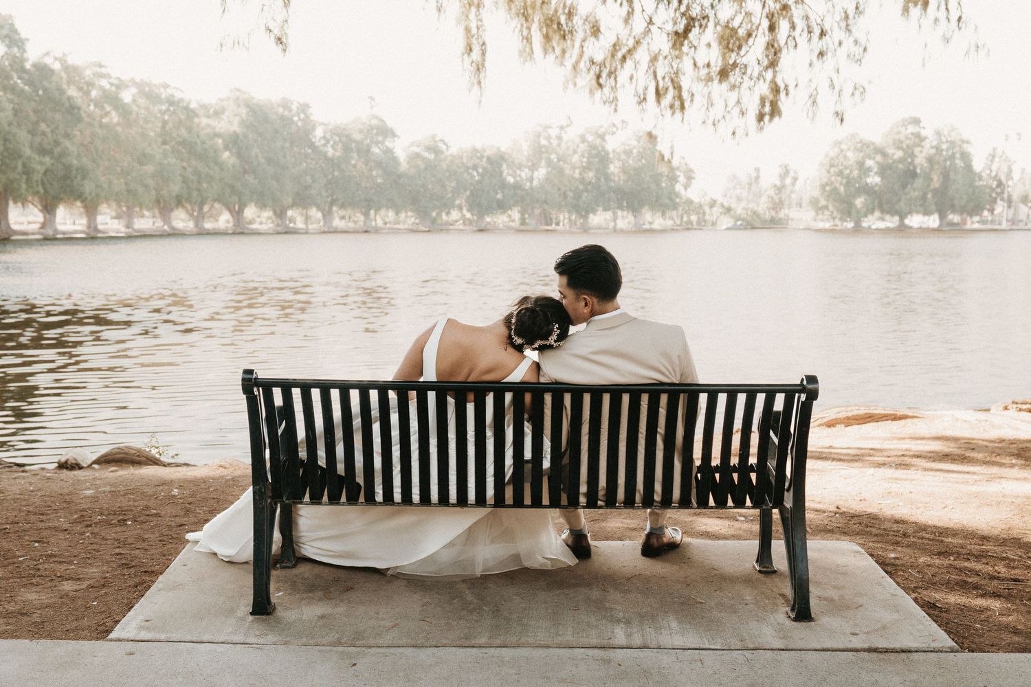 A couple sits together on a wooden park bench overlooking a serene lake on a misty day.