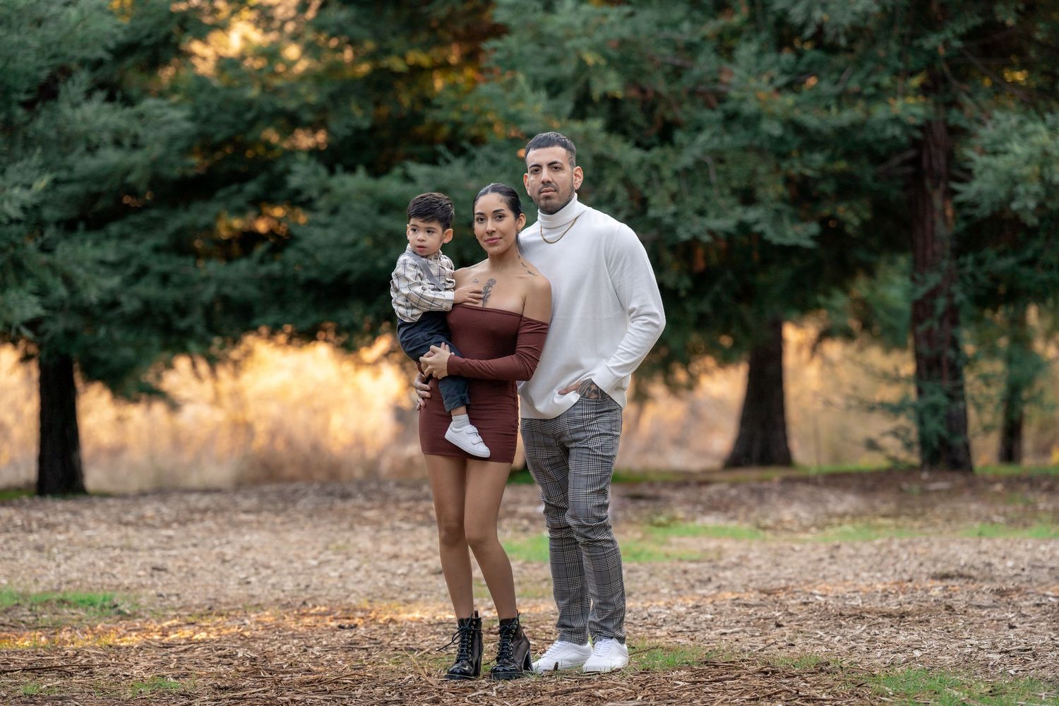 Casual outdoor family photoshoot in a wooded setting with evergreen trees.