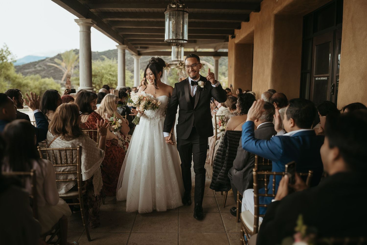 Wedding guests mingle and celebrate in an outdoor covered patio area during a reception gathering.