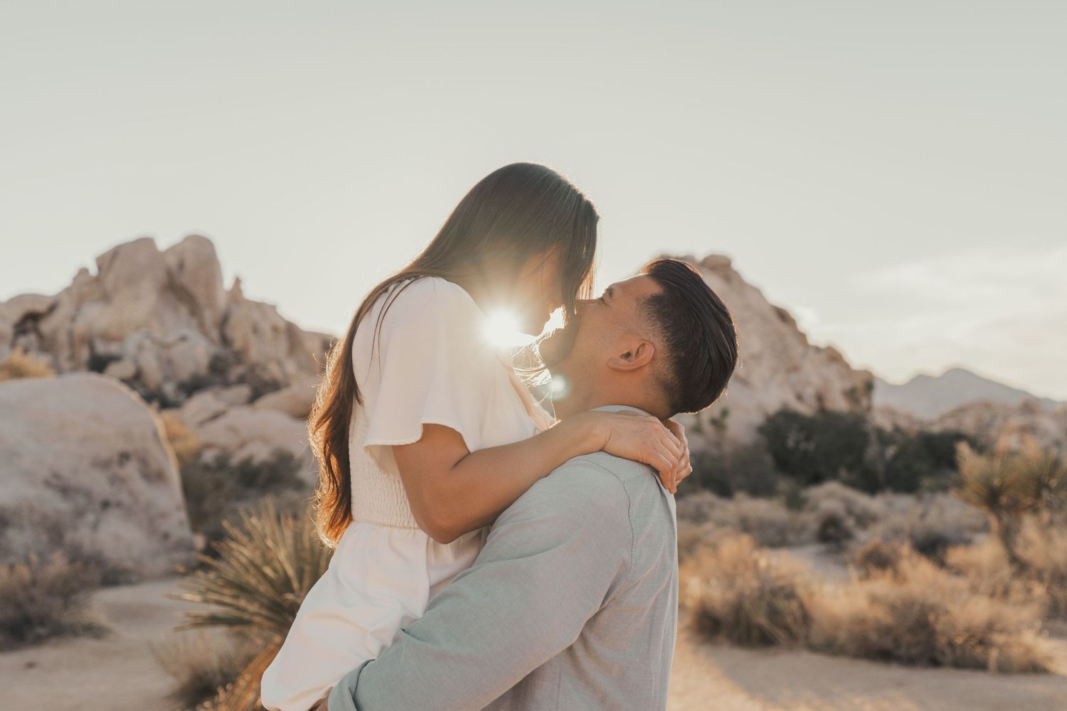 A tender embrace captured against a desert backdrop with sun flare.