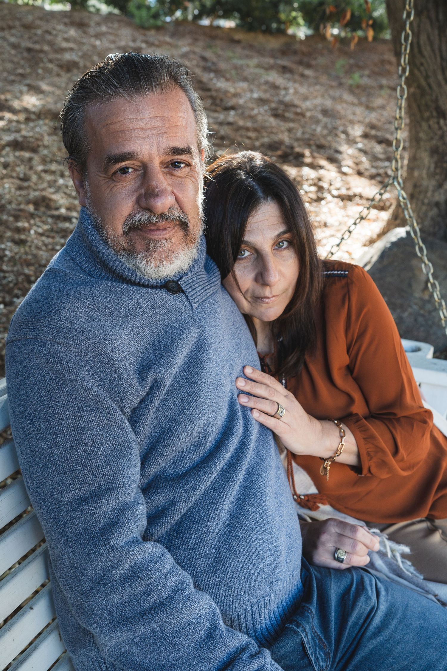 Couple sharing tender moments on park bench wearing casual blue and brown outfits.