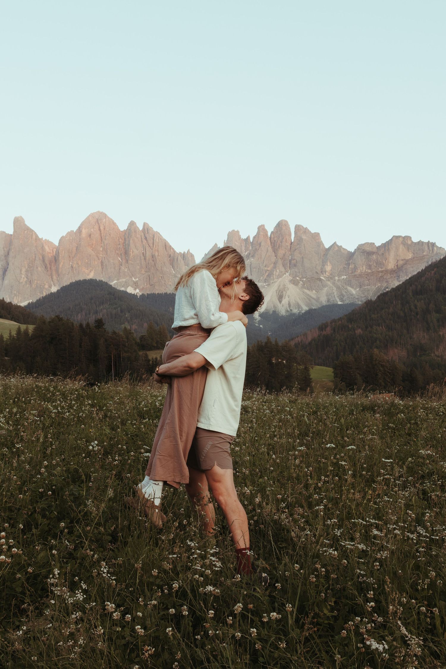 Playful couple dancing in wildflower field with the mountains of Val di Funes behind them.