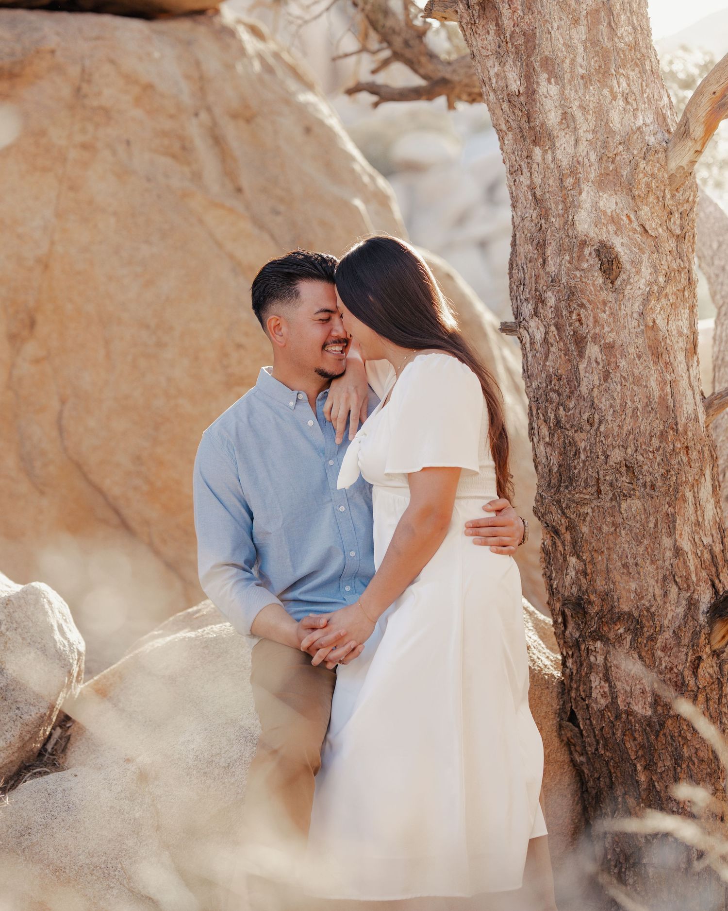 A couple shares a romantic moment near a desert tree with soft lighting.