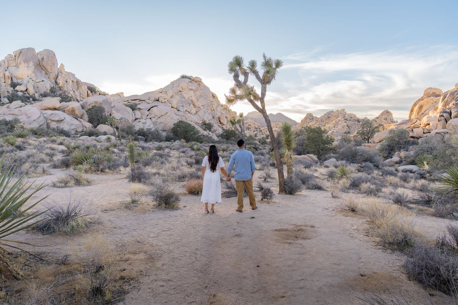 A couple walking hand in hand in Joshua Tree with  rock formations.