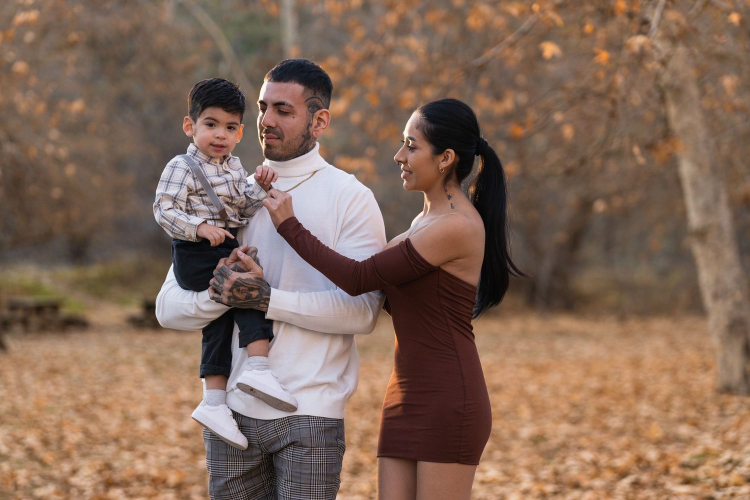 Family walking together through autumn leaves in a park setting during golden hour.