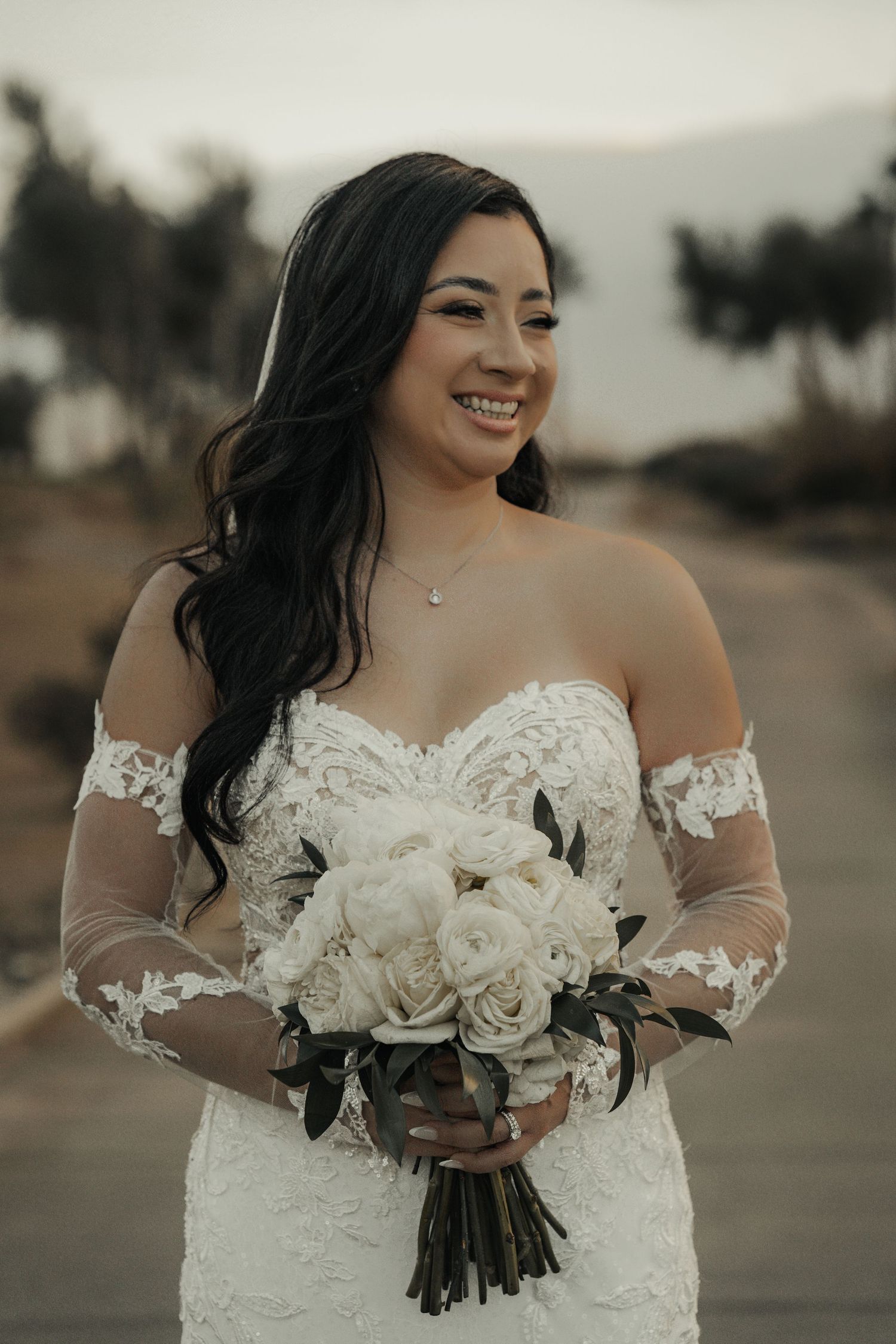 Elegant off-shoulder white wedding dress with lace details and white rose bouquet.
