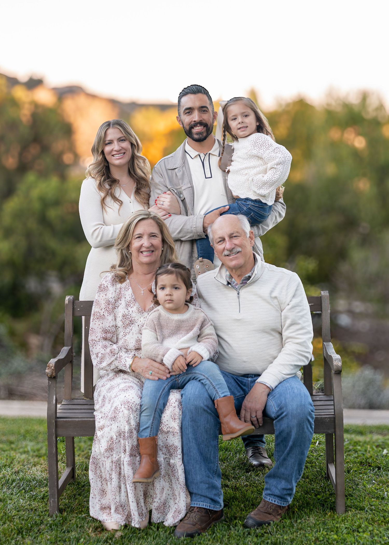 Multi-generational family relaxing together on wooden bench in garden setting.