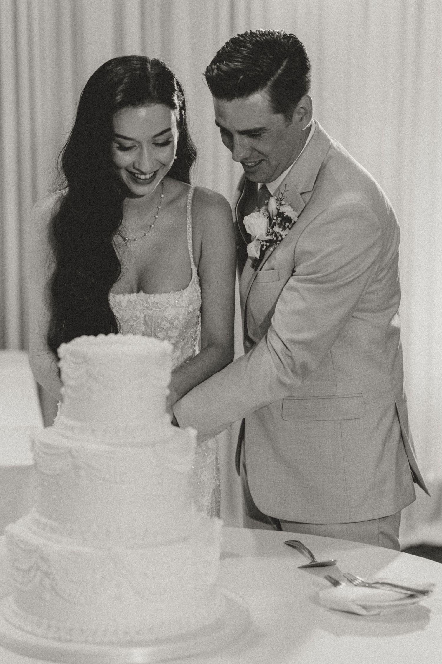 A vintage black and white wedding photo showing a couple cutting their elegant tiered white wedding cake together.
