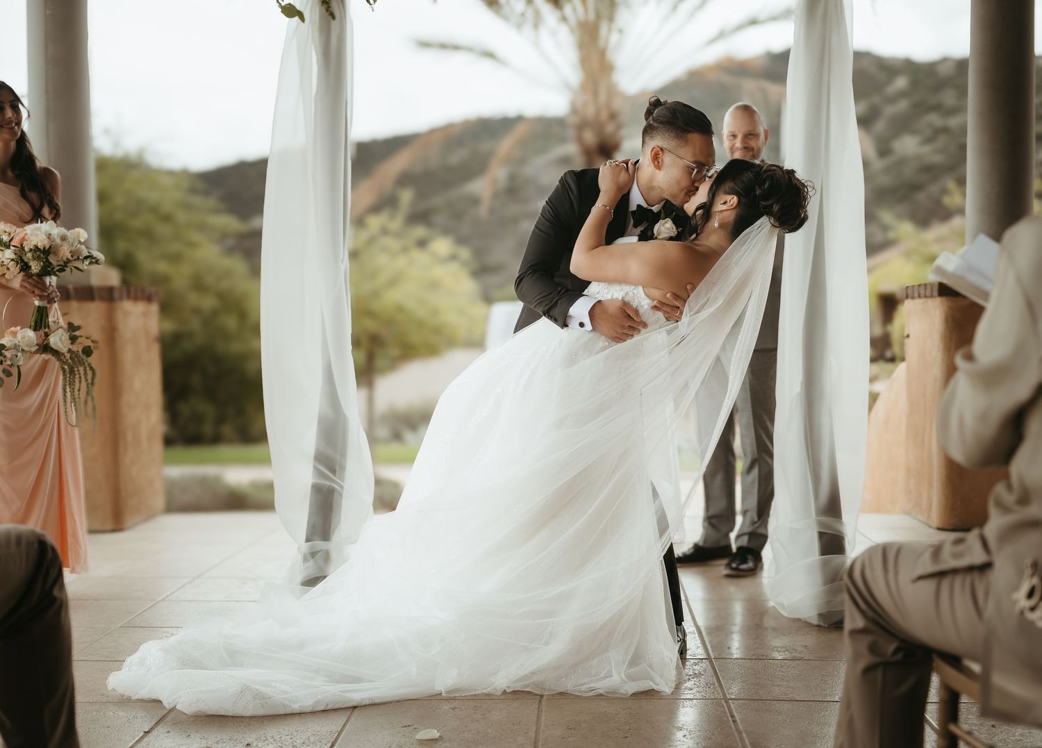 A couple shares a romantic moment on their wedding day in an elegant outdoor venue with mountains in the background.