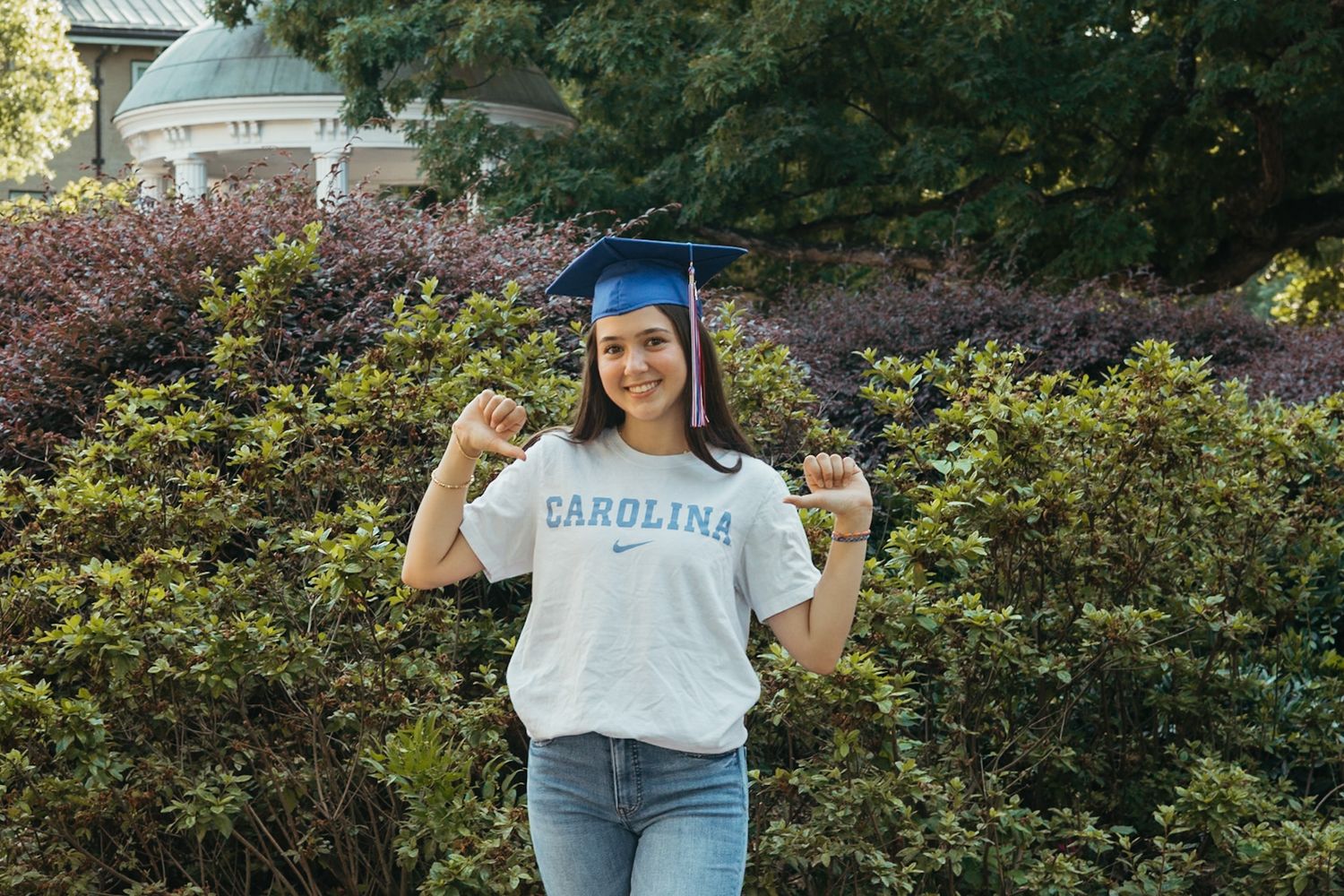 Graduate in Carolina blue shirt and graduation cap celebrating on campus.