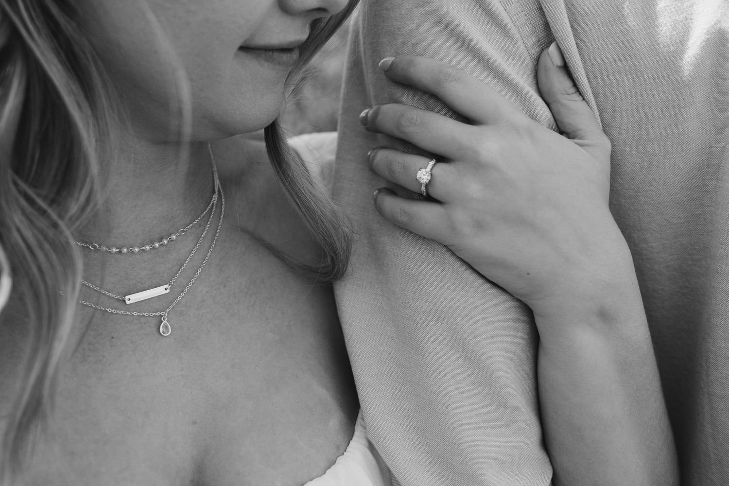 Close-up black and white photo of jewelry and hands showing romantic embrace.