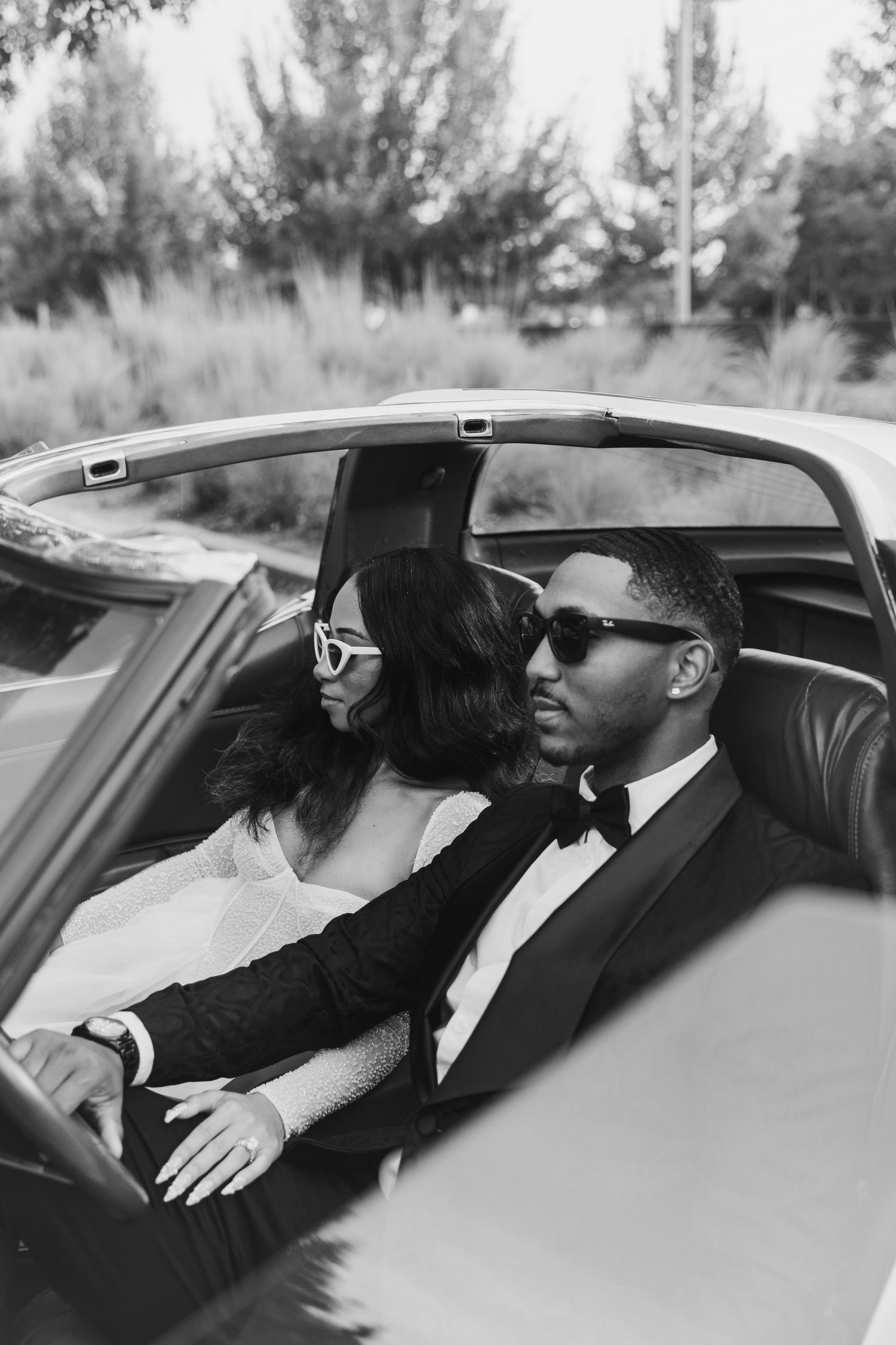 Black and white photo of a couple in formal attire seated in a classic car.