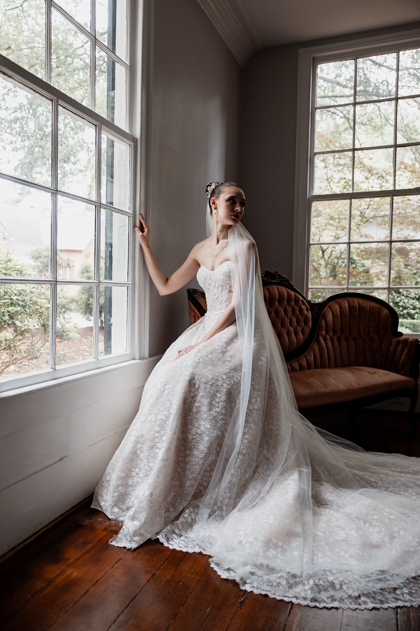 Elegant lace wedding gown with long train photographed by large windows in a vintage room.