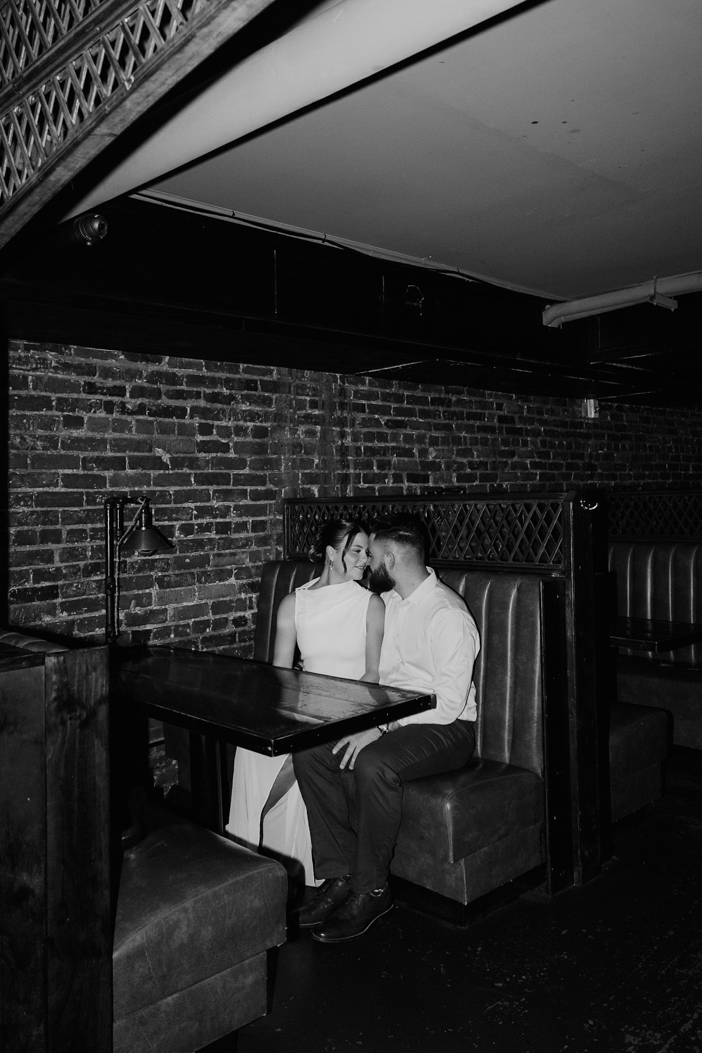Artistic black and white photo of couple sharing intimate moment in industrial brick venue.