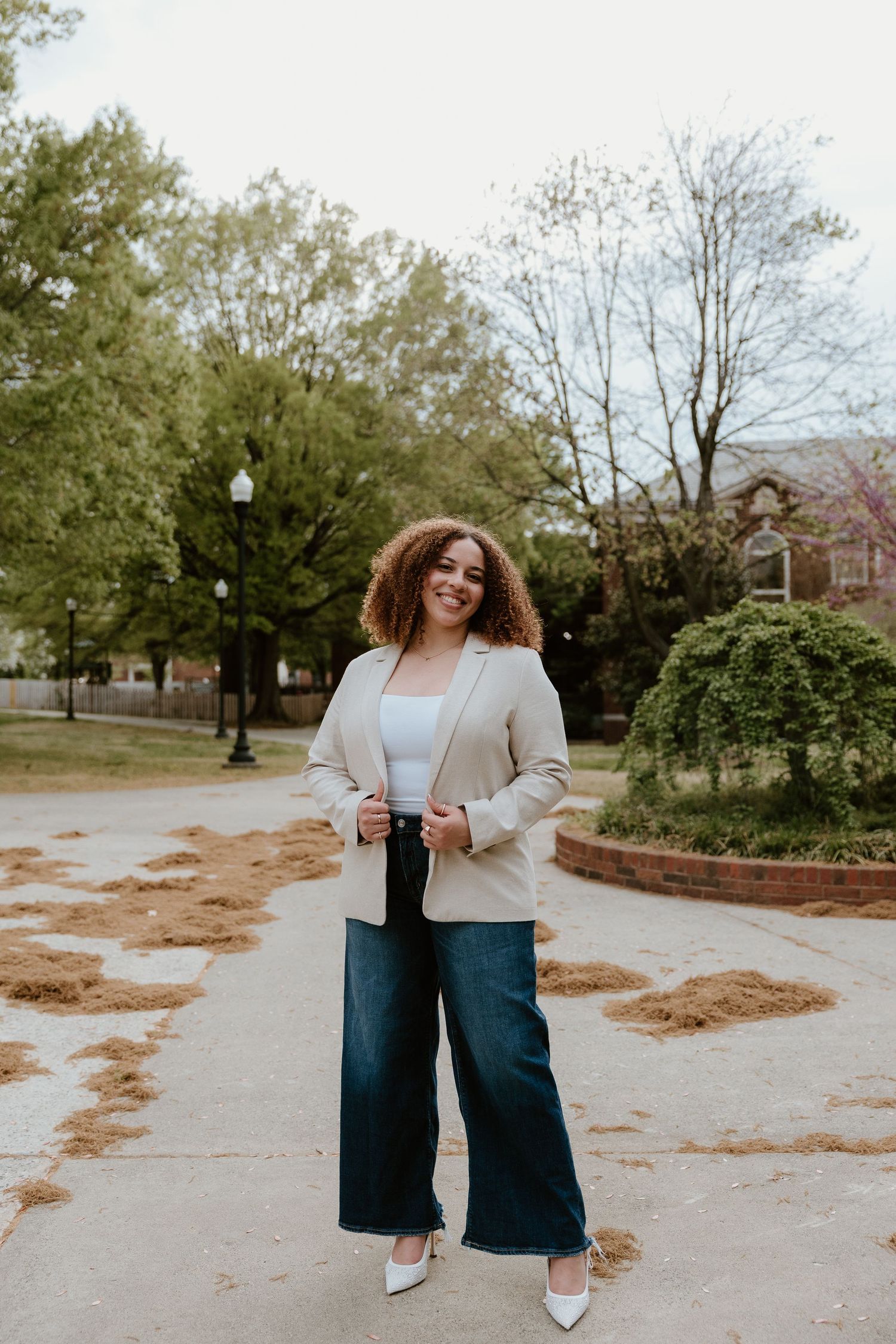 Stylish outfit featuring wide-leg jeans, white top, and beige blazer on a tree-lined pathway.