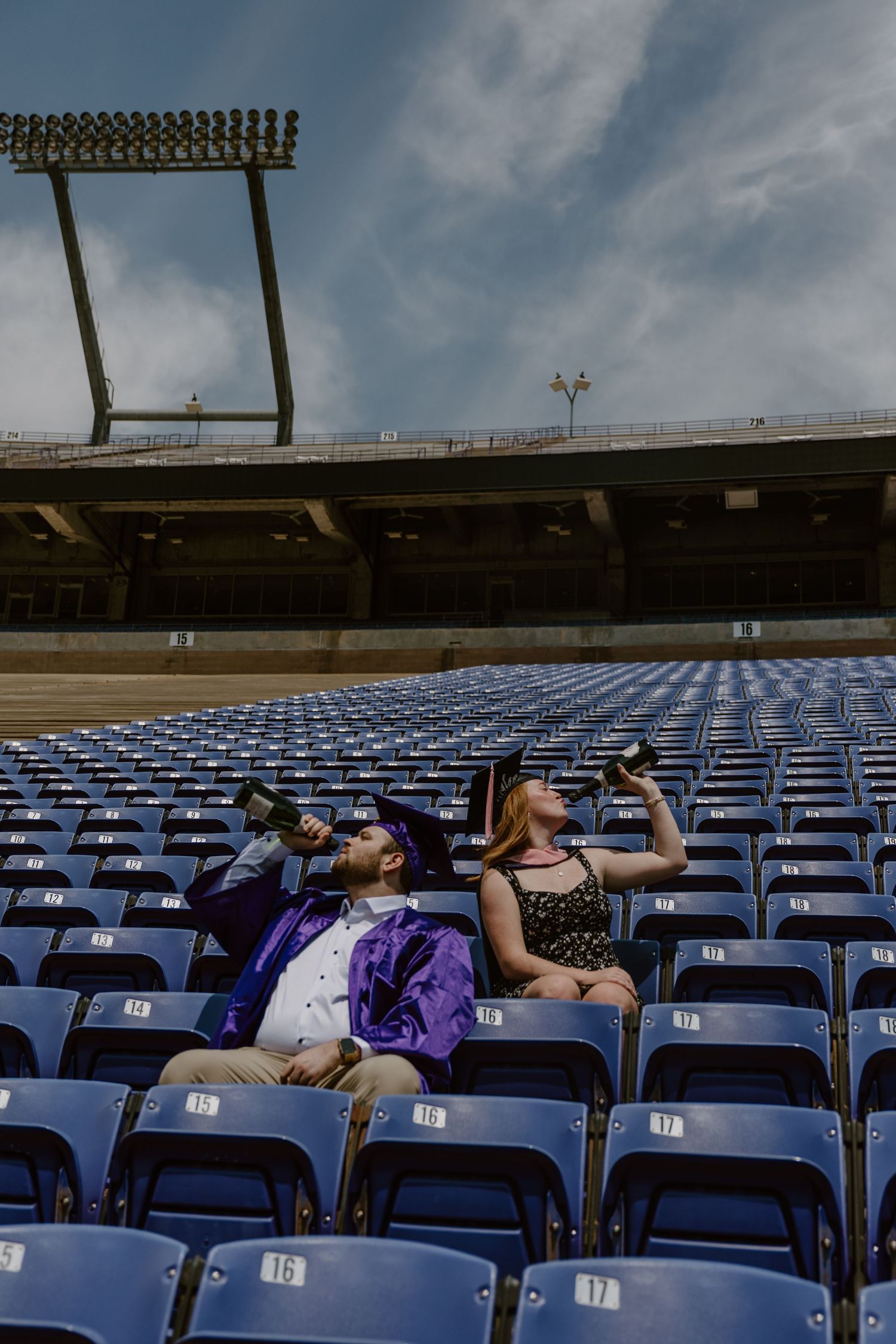 Wide view of stadium bleachers with blue seats under cloudy skies.