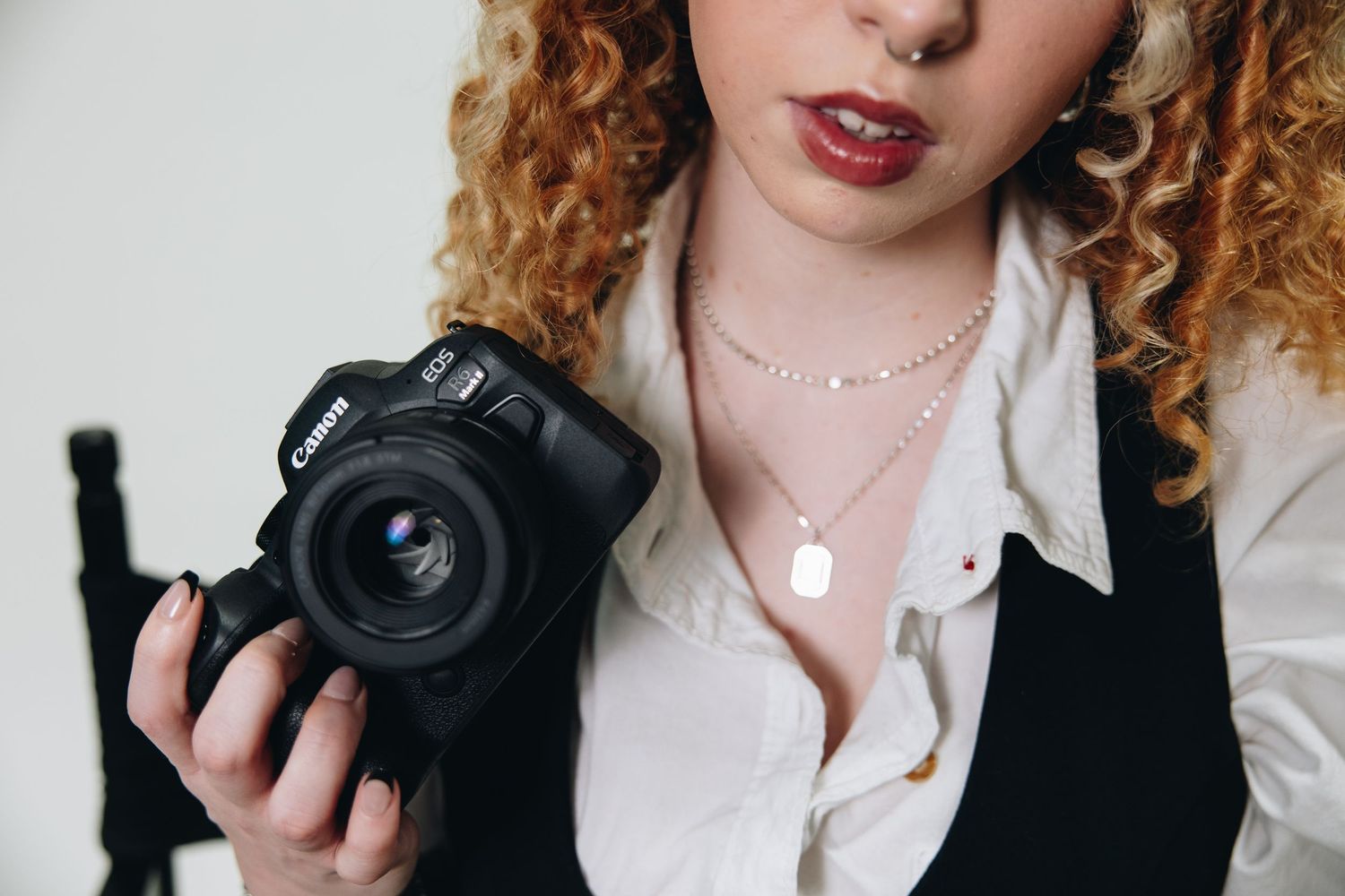 Close up of photographer holding professional camera wearing black blazer and white shirt.