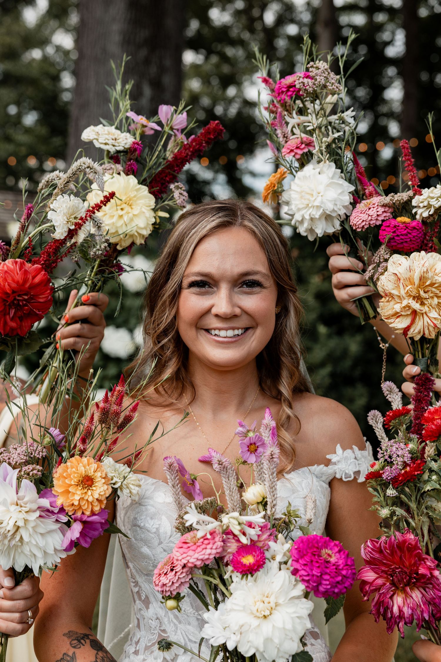 A wedding portrait featuring vibrant floral bouquets with pink, white, and red blooms in a lush outdoor setting.