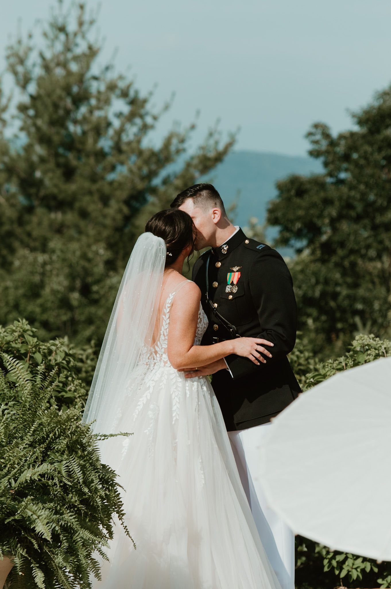 Bride and groom embrace during mountain wedding ceremony with flowing veil.