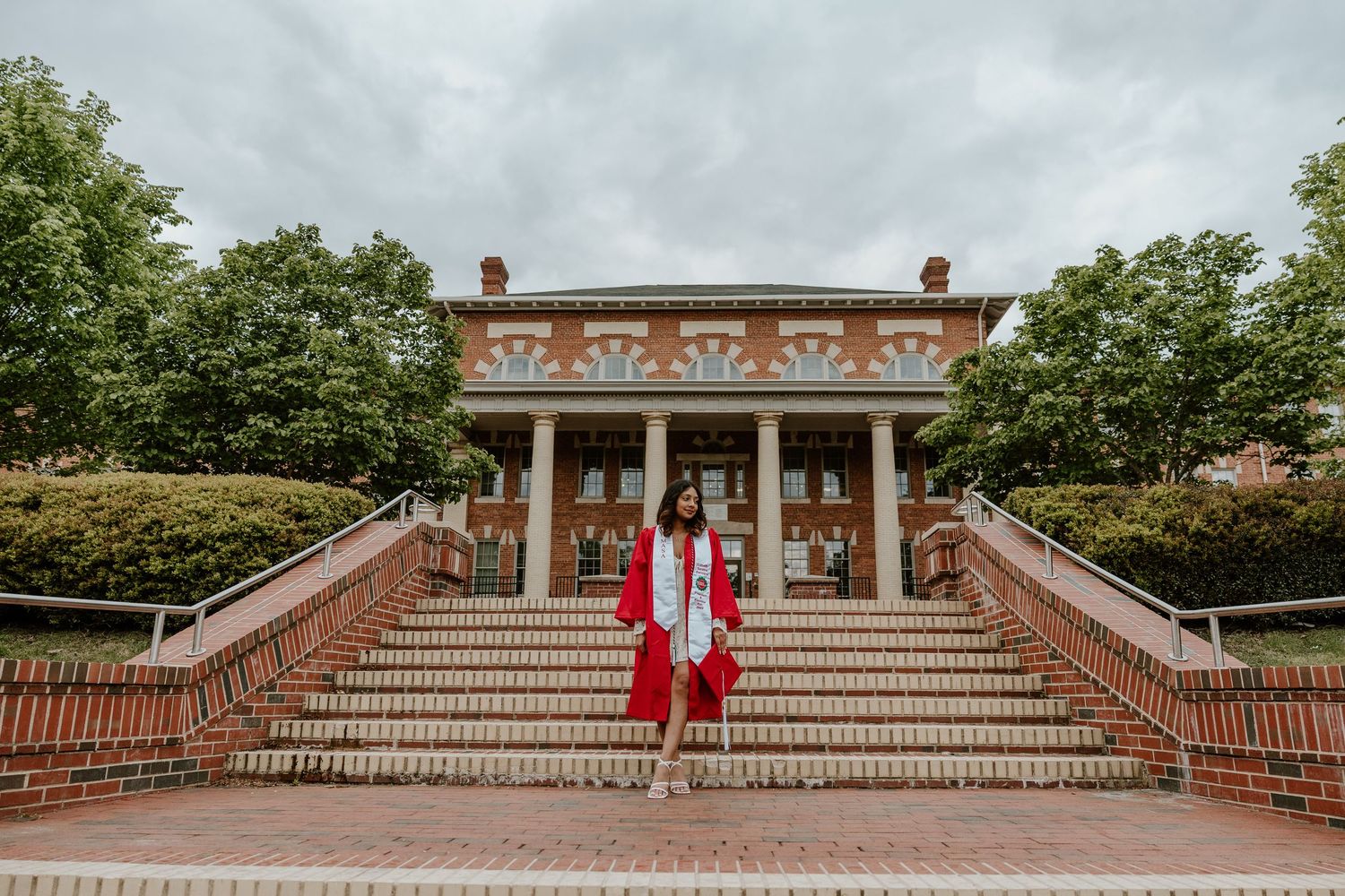 Person in red outfit standing on grand brick steps of historic colonial-style building.