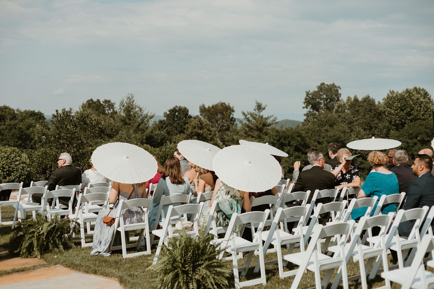 Outdoor wedding ceremony setup with white chairs and parasols under blue sky.