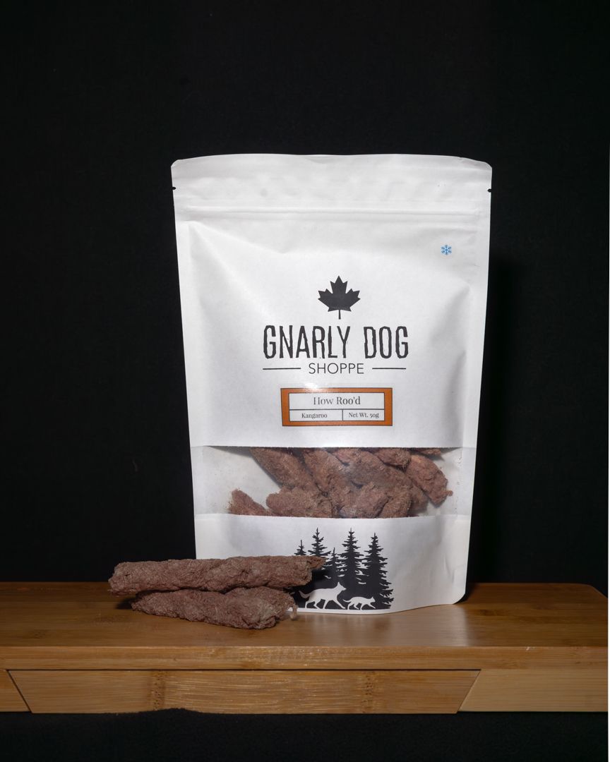 White resealable bags of artisanal beef jerky displayed on a wooden surface against a dark background.