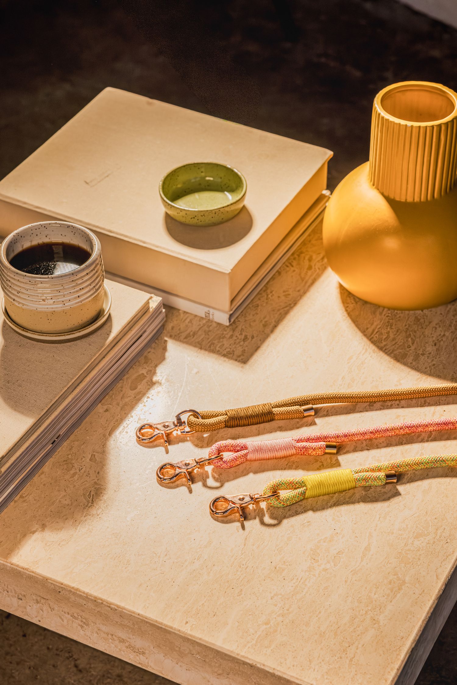 Colorful dog leashes with rose gold clips displayed on a marble tray beside a yellow vase, books, and ceramic cups.