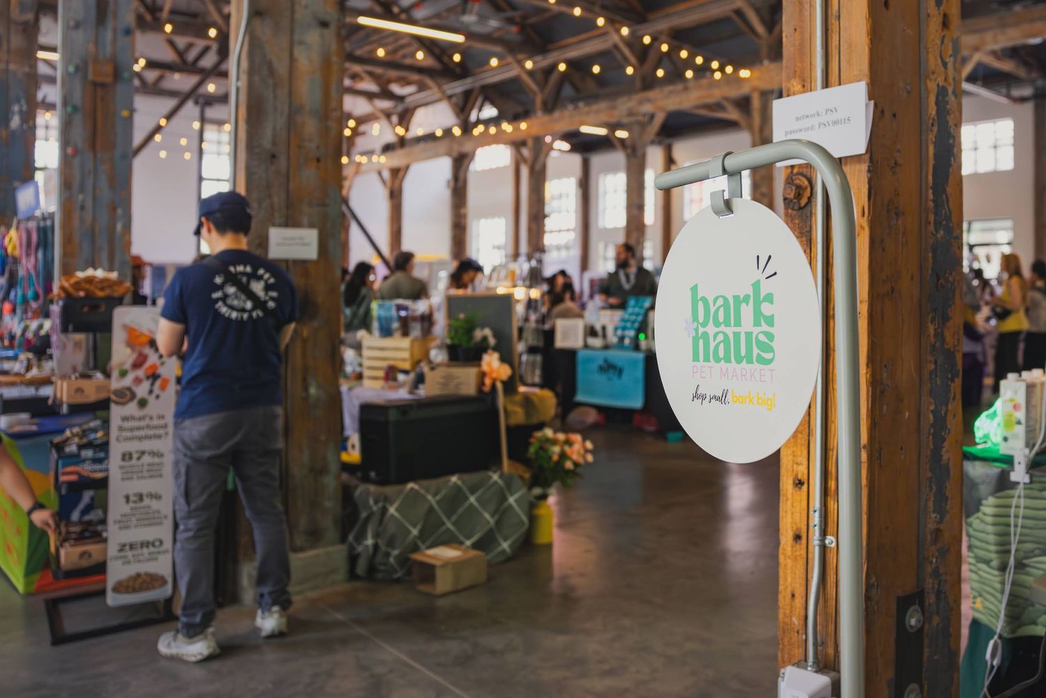 Bark Haus pet market event inside a rustic barn venue with vendors and shoppers browsing dog products.