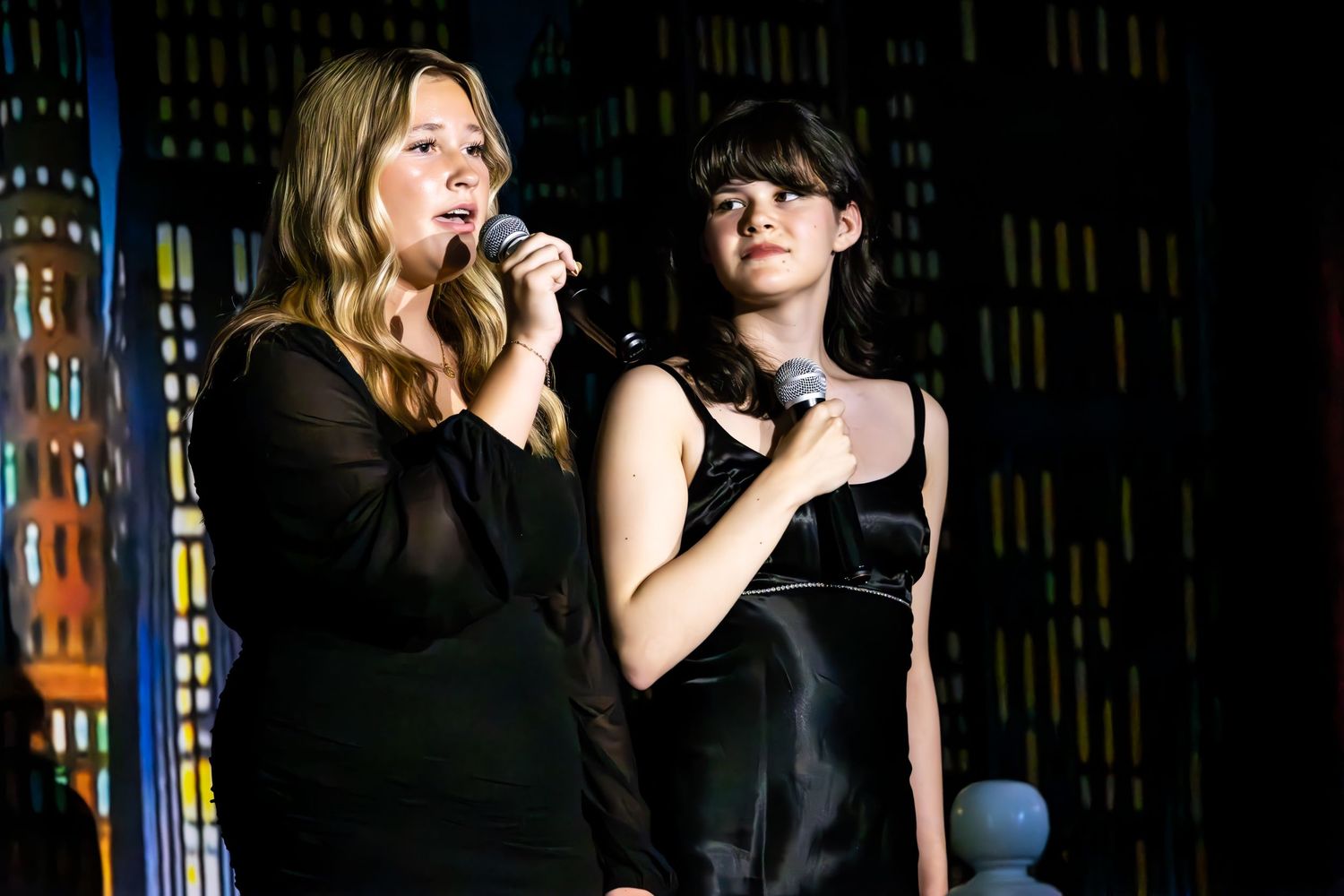 Performers singing on stage in front of a dark background with colorful illuminated strips.