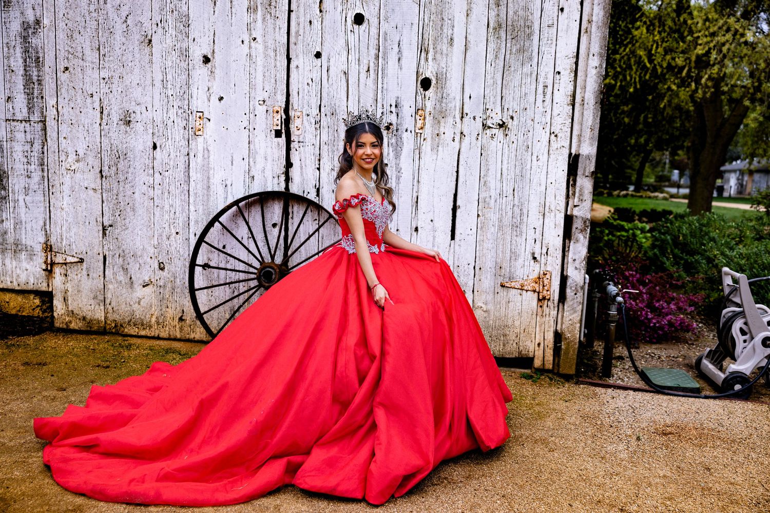 A stunning red ball gown flows dramatically across rustic outdoor settings with weathered wood backgrounds.